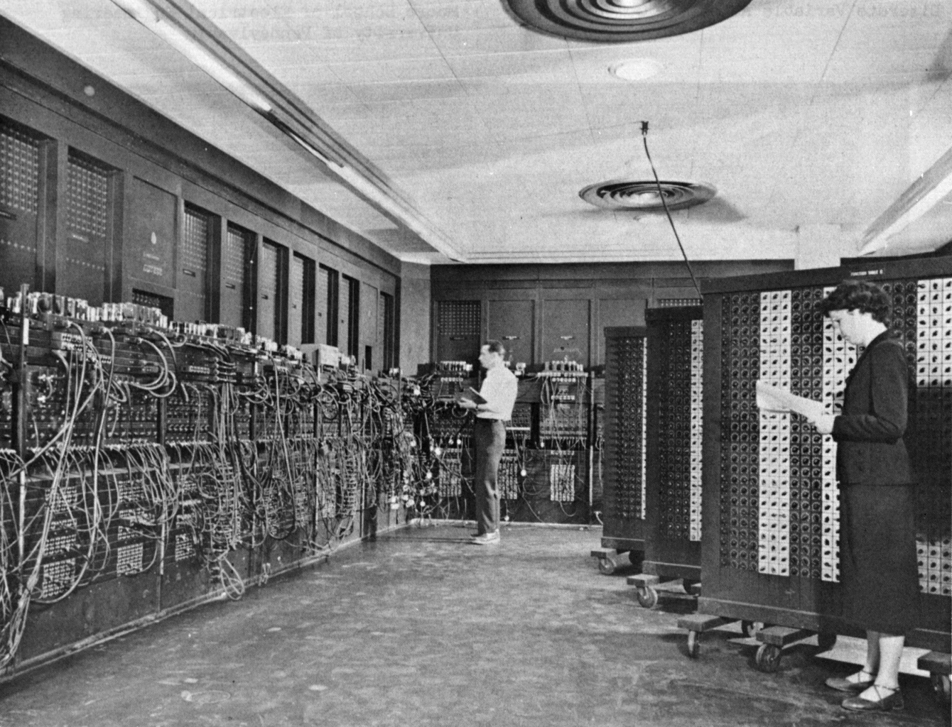 Glen Beck and Betty Snyder programming the ENIAC computer at the Ballistic Research Laboratory in 1946. Two operators stand among floor-to-ceiling racks of vacuum tubes.